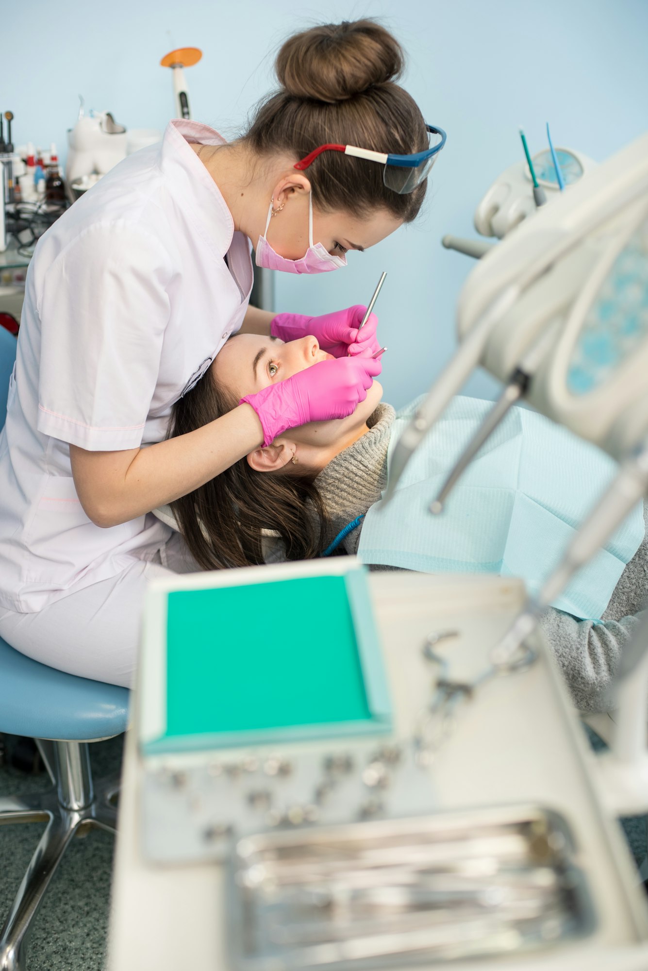 Female dentist with dental tools - mirror and probe treating patient teeth at dental clinic office